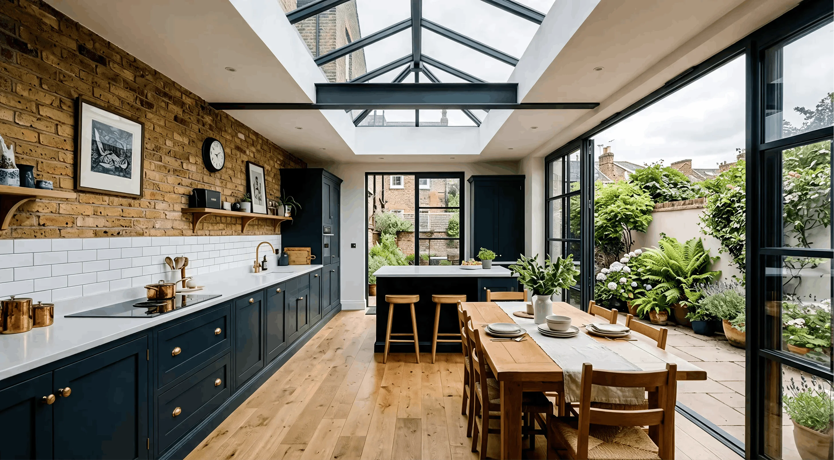 The finished navy kitchen and dining room with oak flooring, an exposed brick wall carrying open shelving, and doors open onto the garden terrace