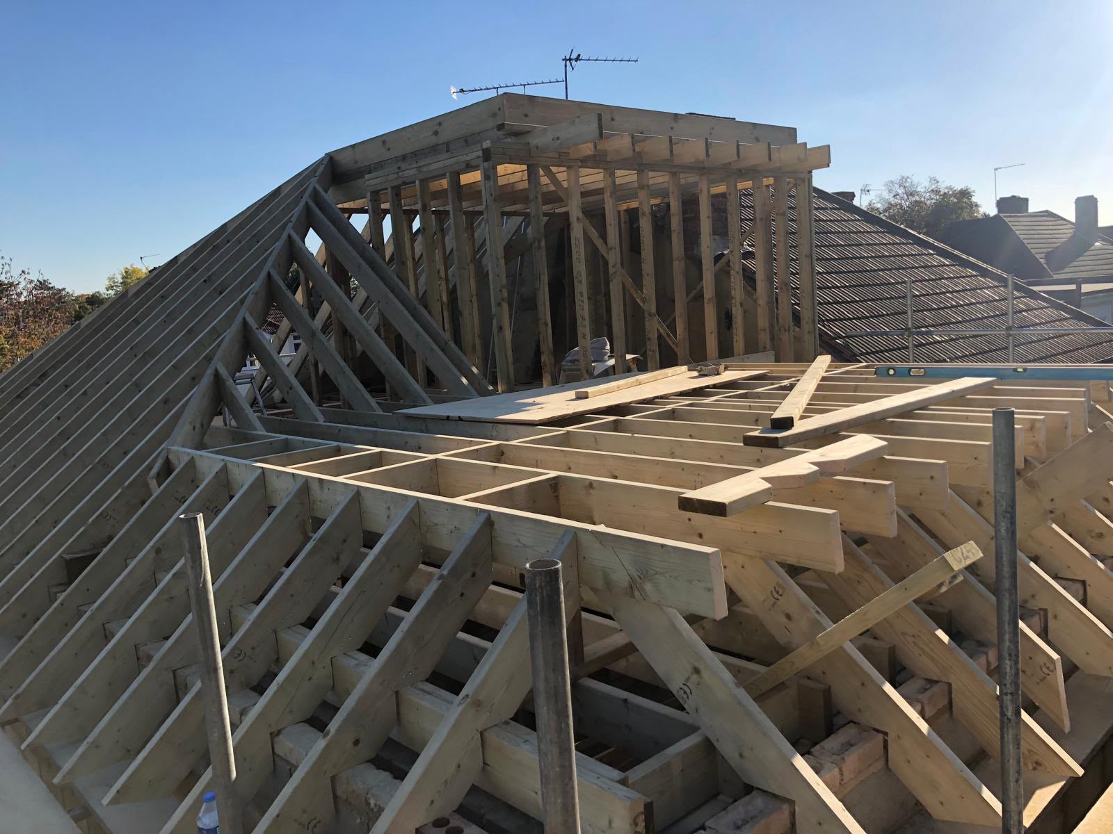 A timber roof frame with hip rafters, new floor joists and a framed dormer box under a clear blue sky