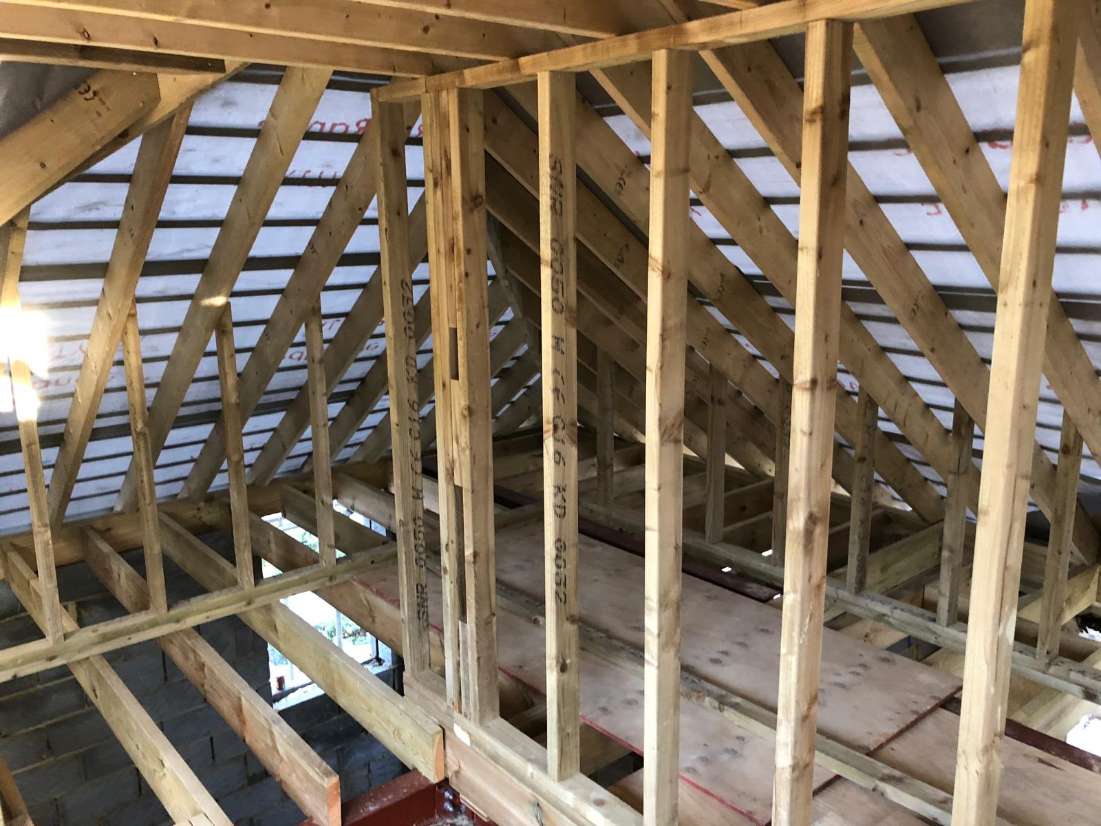 Inside a new roof structure with timber rafters, stud walls and membrane, above a boarded loft floor