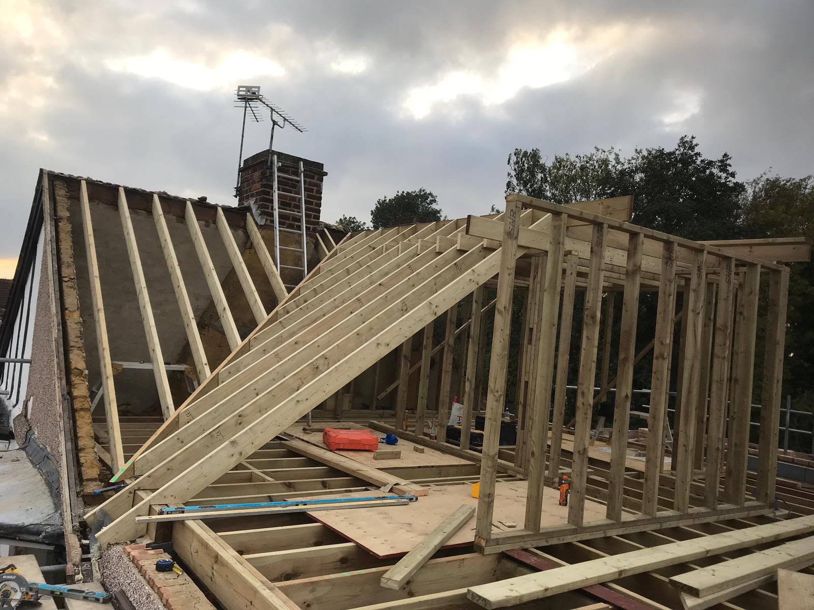 New rafters running up against an existing roof and brick chimney, with a timber stud wall for a dormer standing on the loft floor