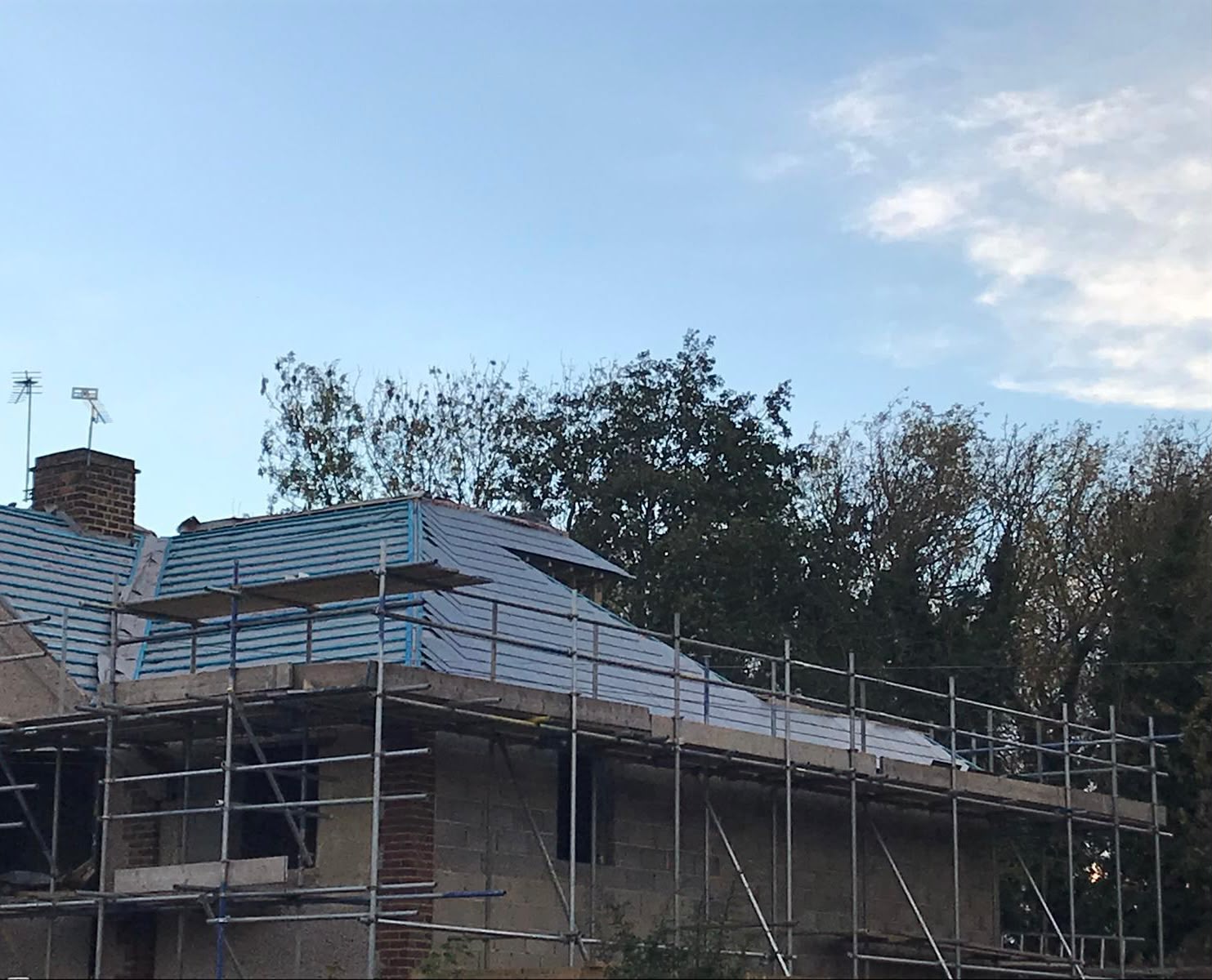 A new hipped roof covered in grey membrane and blue battens behind scaffolding, with a dormer on the rear slope and blockwork walls below