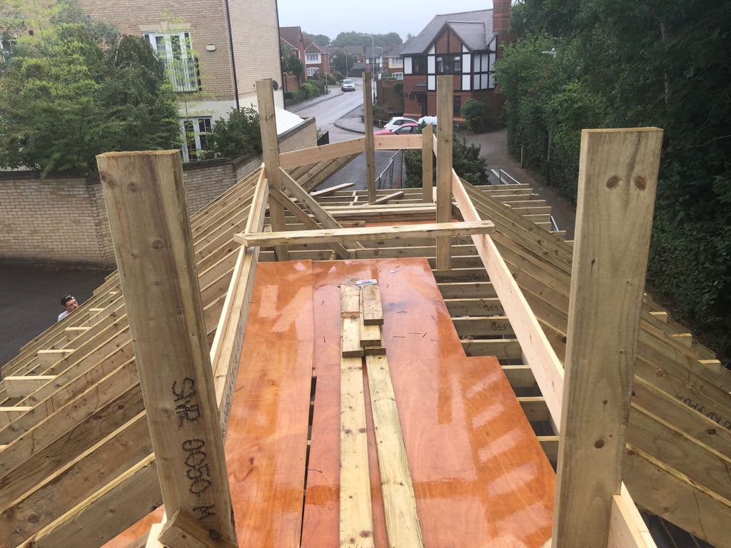 Looking along a garage roof being framed in timber, with a plywood deck in the centre and a residential road beyond