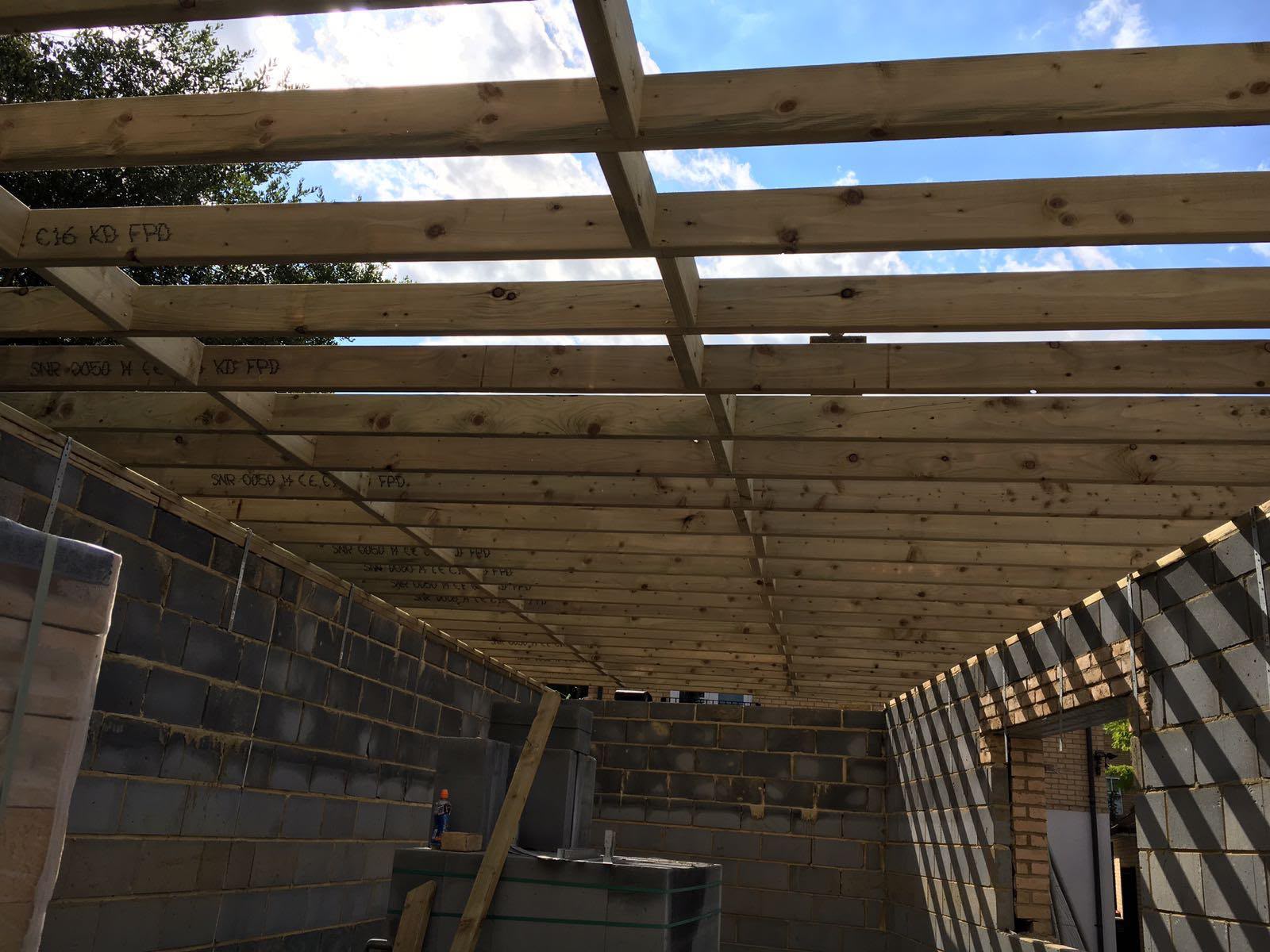 Timber ceiling joists spanning between blockwork walls inside a garage under construction, with sky showing between them