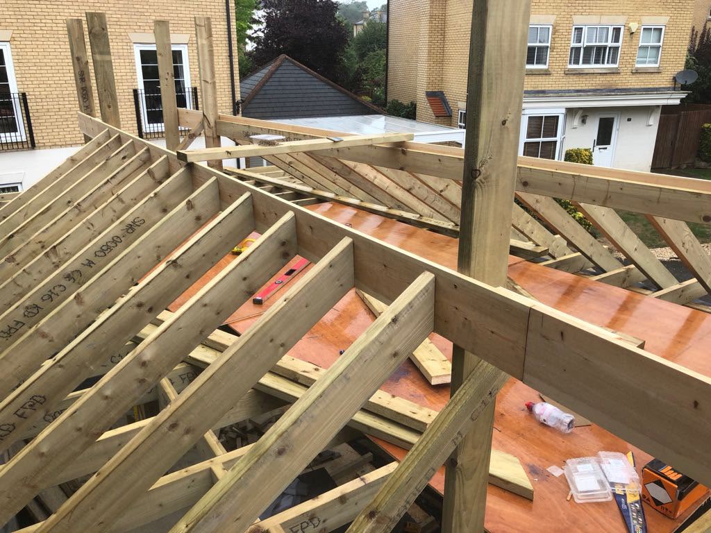 Close view of new timber rafters and hip boards on a garage roof, with brick houses beyond