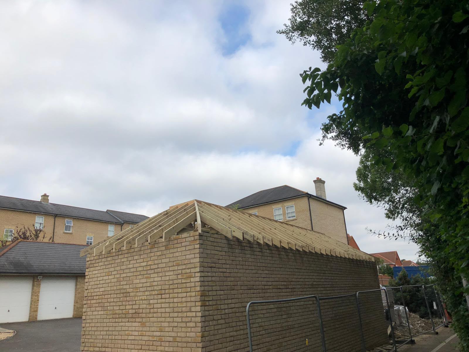 A new yellow brick garage with its hipped timber roof framed, beside a row of houses and existing garages