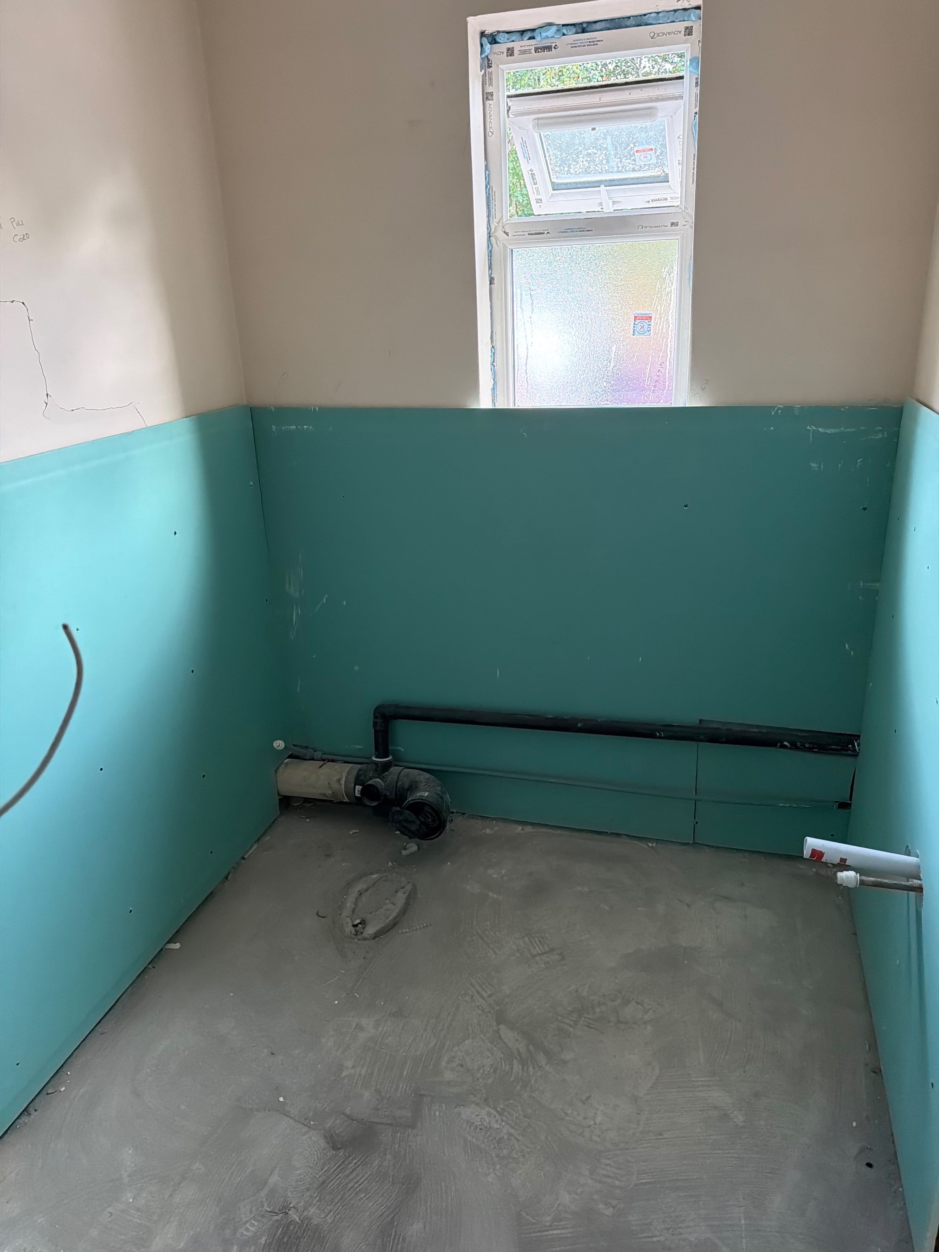 The same small room with turquoise boards fixed over the lower walls and the black waste pipe running in front of them
