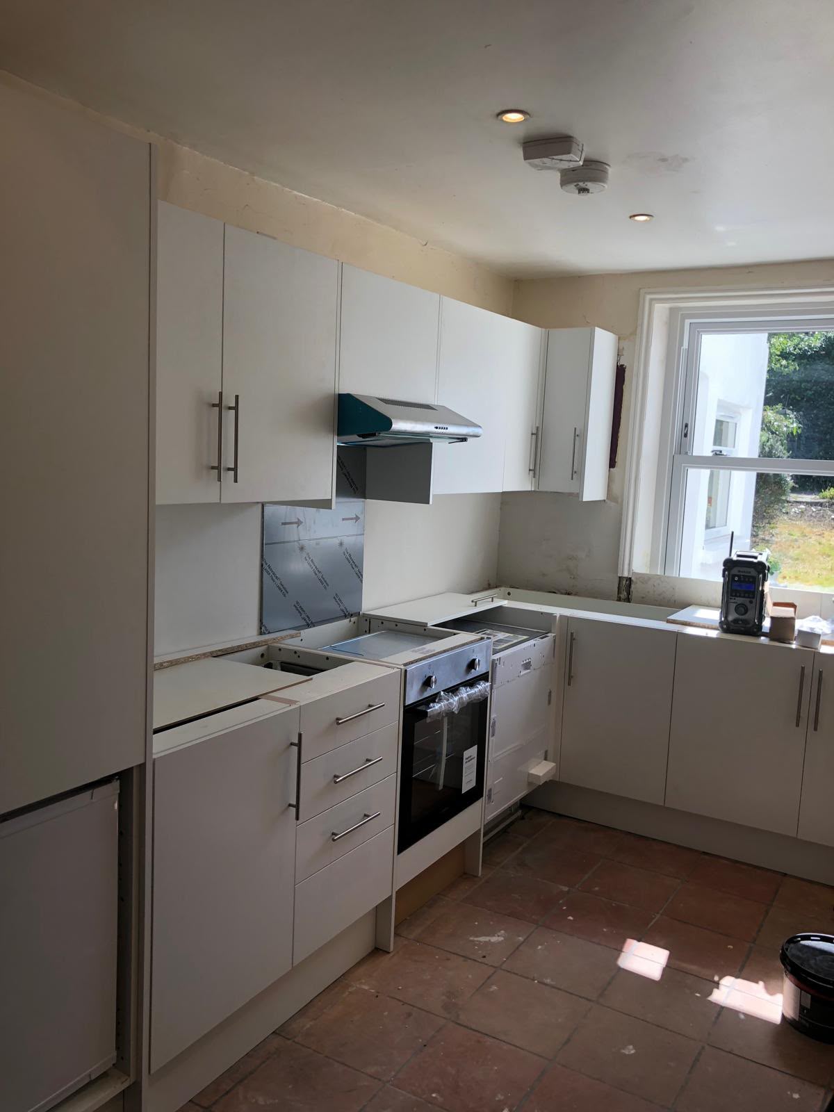 White kitchen units with a built-in oven and integrated dishwasher fitted, an extractor hood above and the worktops not yet in place