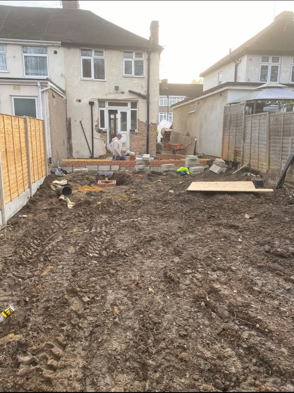A cleared garden with the first brick courses of a new extension laid out against the back of a house