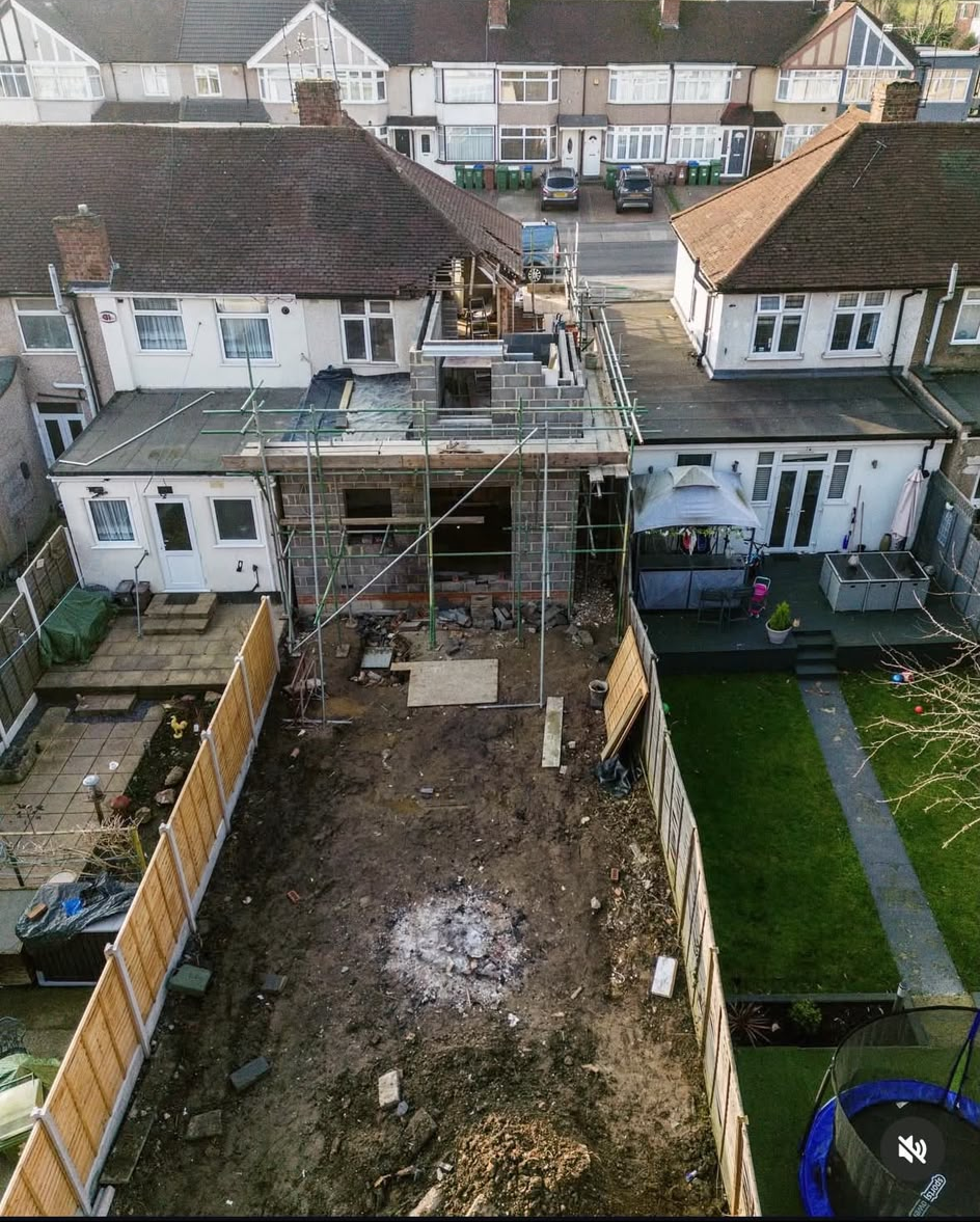 Wide aerial view over a house with a blockwork extension and scaffolding, looking across to the street and the houses opposite