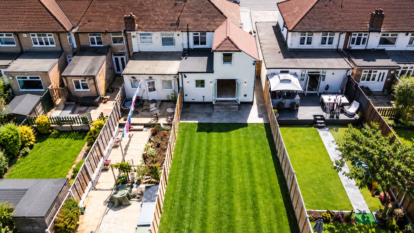 Aerial view of a finished white-rendered two-storey side and single-storey rear extension on an end-of-terrace house, with a new patio and a long striped lawn