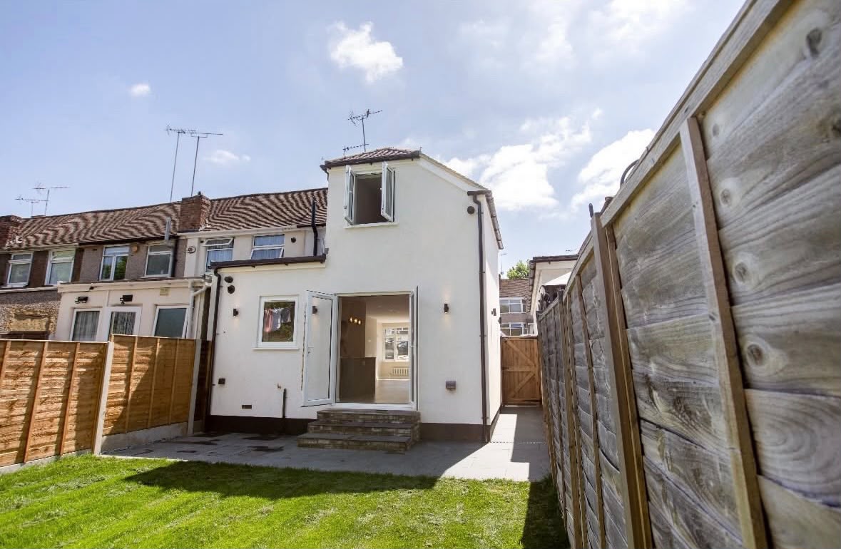The white-rendered rear of a house with a two-storey side extension and a single-storey rear extension, French doors and brick steps onto a new patio and lawn