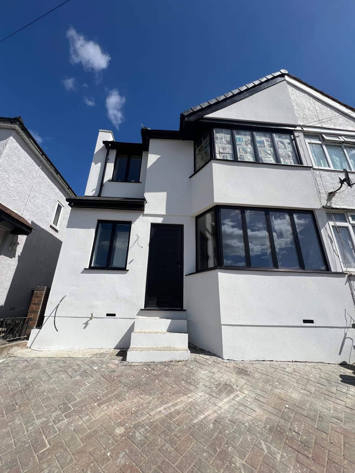 A freshly rendered white semi-detached house with a side extension, black framed windows and a new front door above a block-paved drive