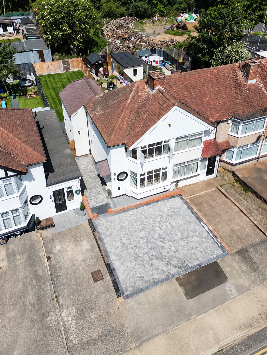Aerial view of a white semi-detached house with a tiled hipped roof, a side extension and a newly block-paved front drive