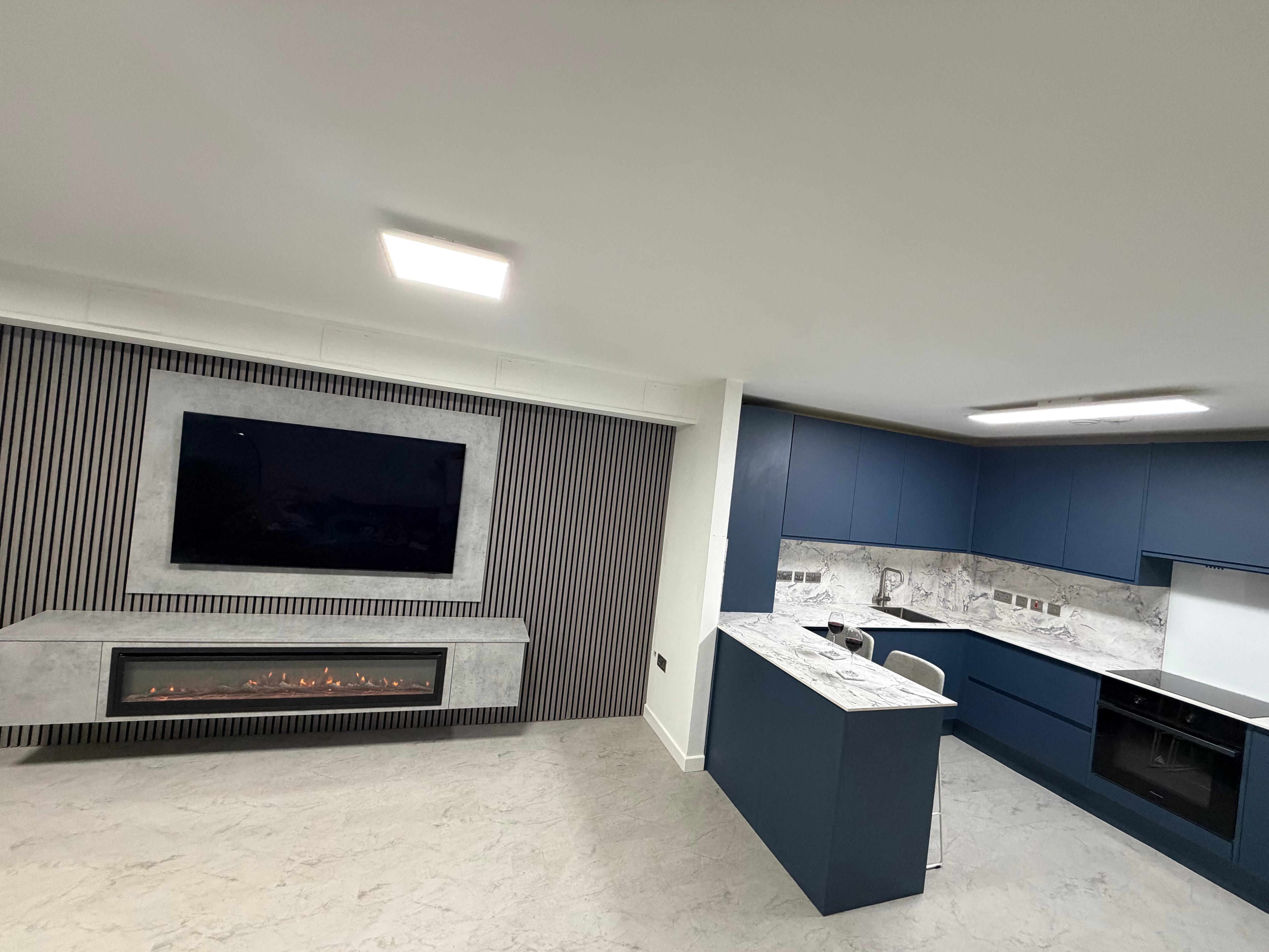 Renovated open-plan room with a navy kitchen, marble-effect worktops and a slatted media wall with a built-in fire