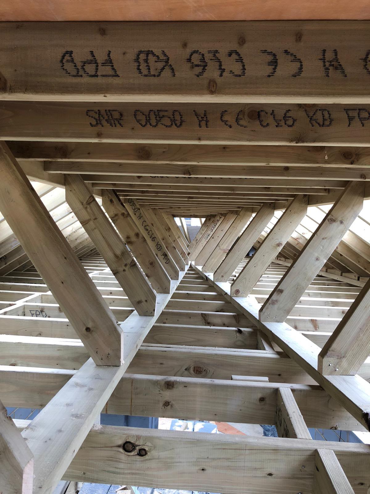 Looking up into a new timber hipped roof, with hip and jack rafters meeting over the ceiling joists